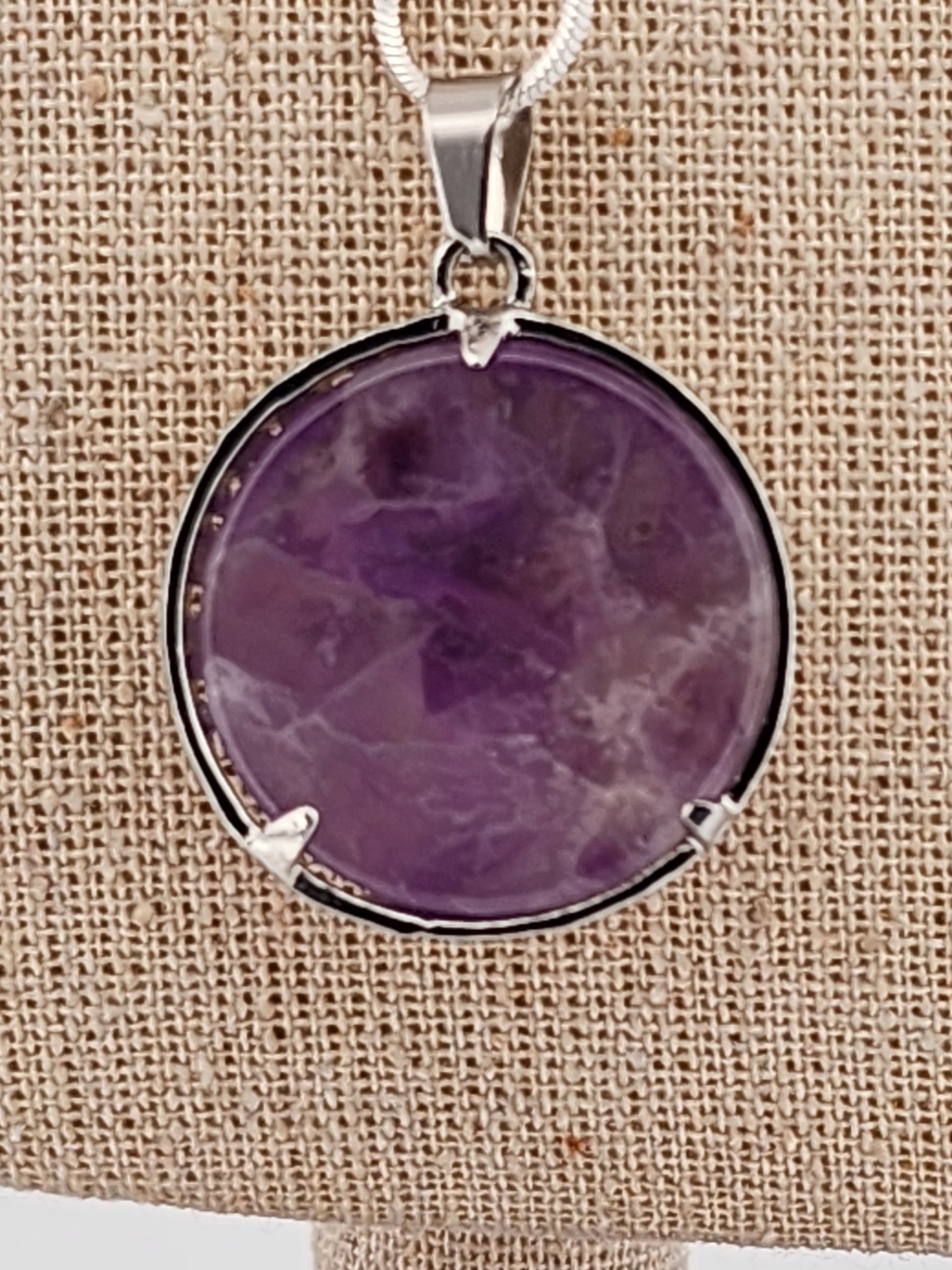 Purple stone pendant on a beige fabric background