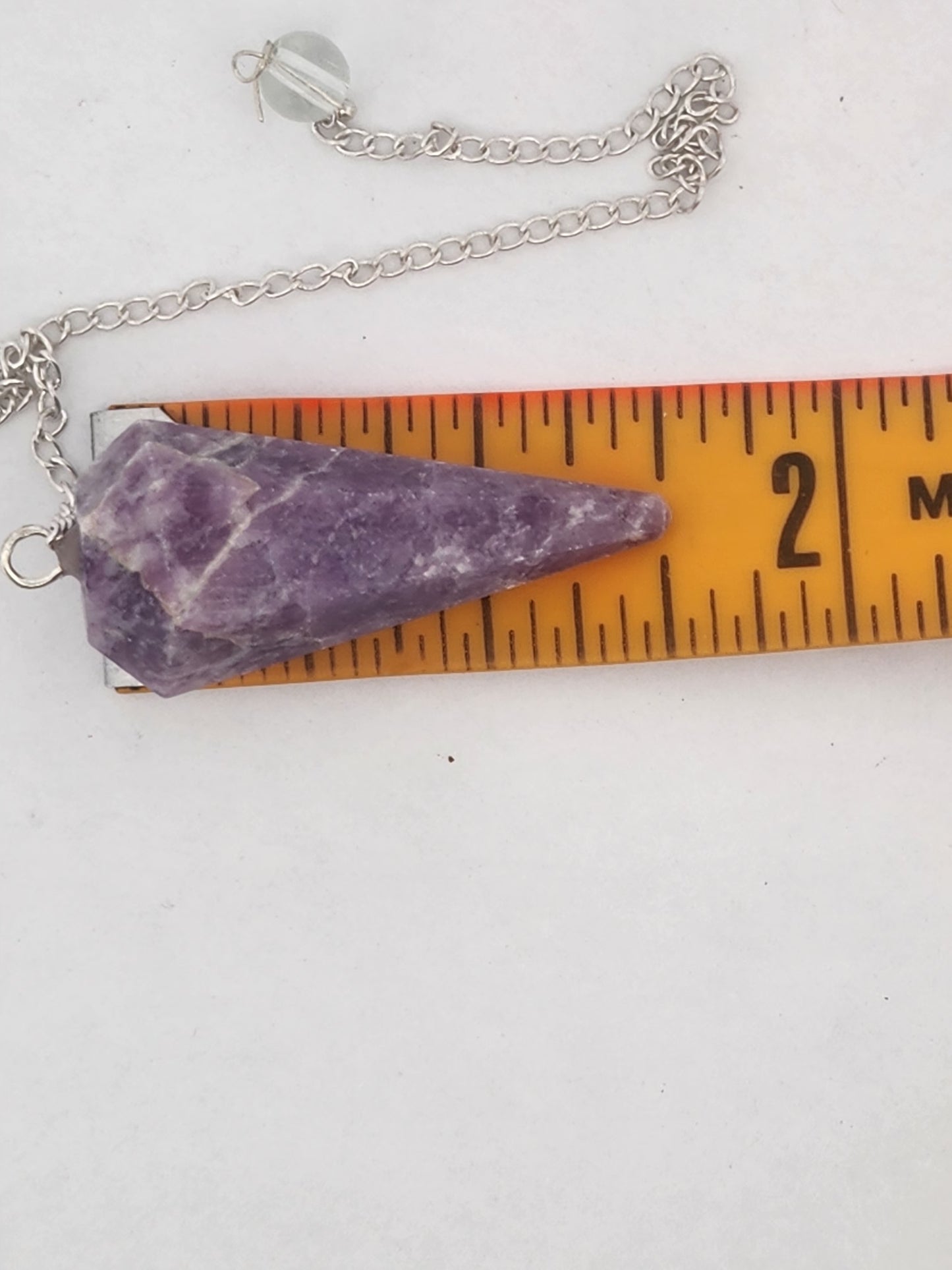 Purple stone pendant on a chain with a ruler for scale on a white background