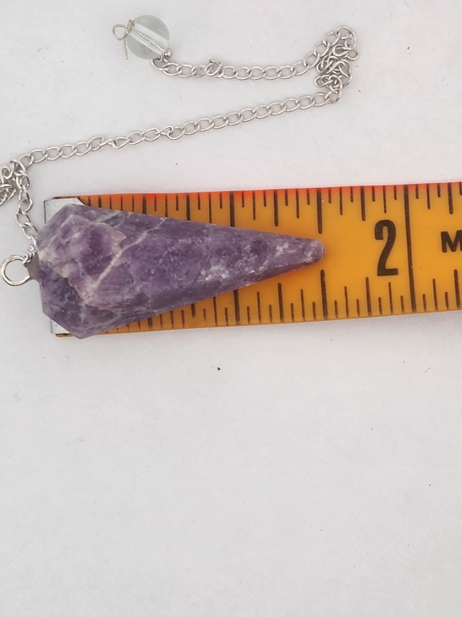 Purple stone pendant on a chain with a ruler for scale on a white background