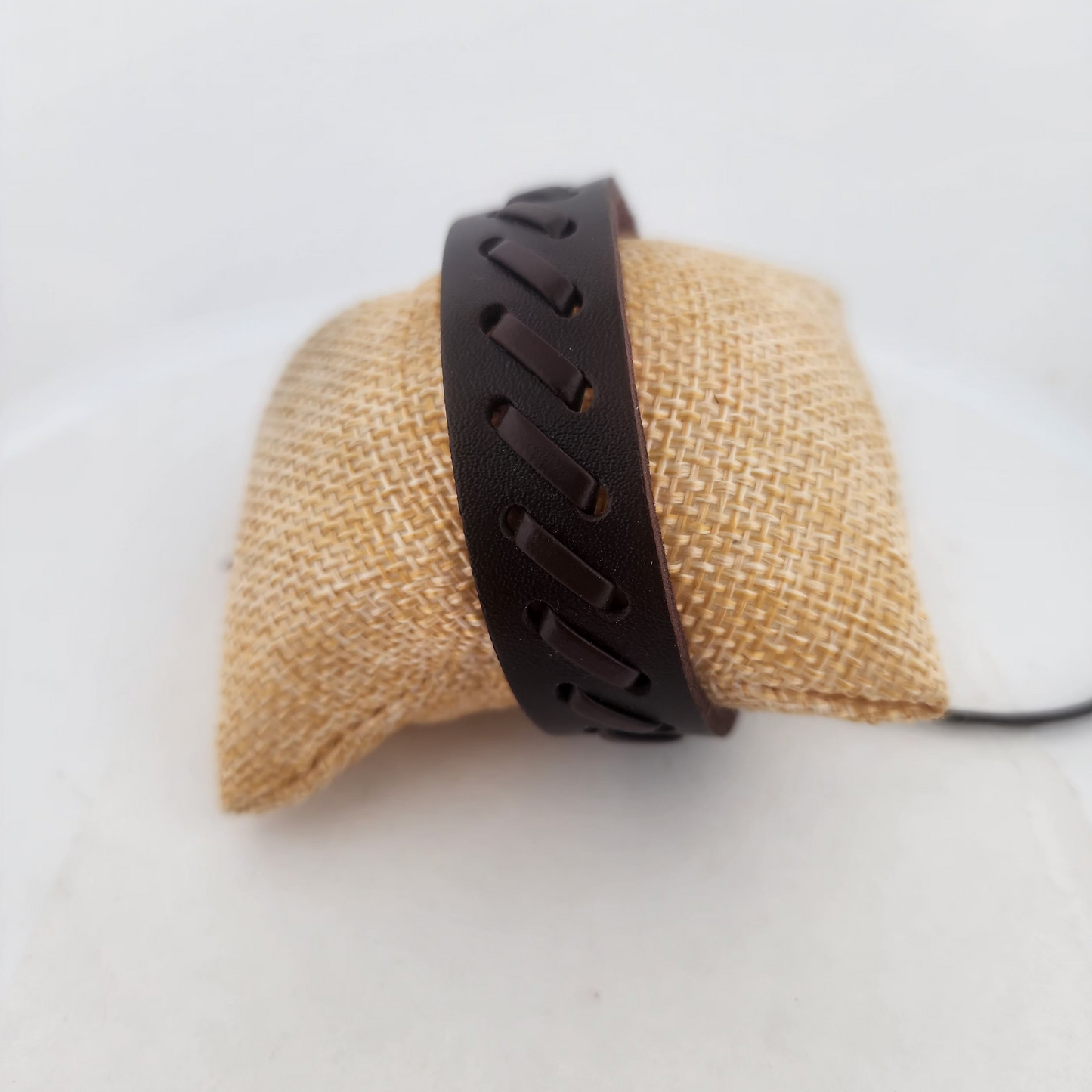 Brown leather bracelet on a burlap-covered block against a white background