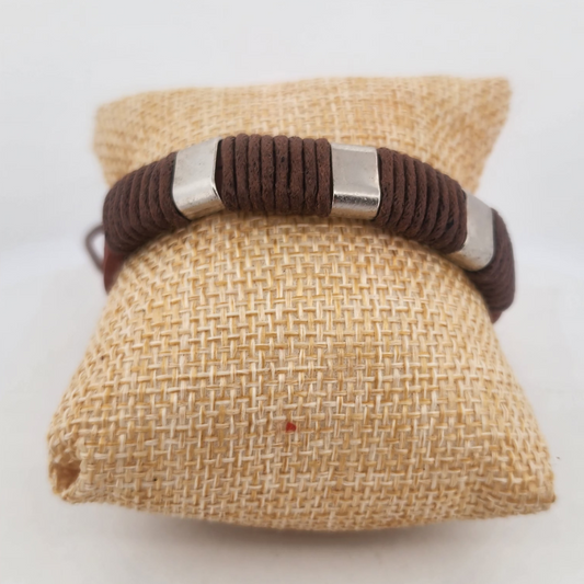 Brown braided bracelet with silver accents on a beige fabric pillow against a white background