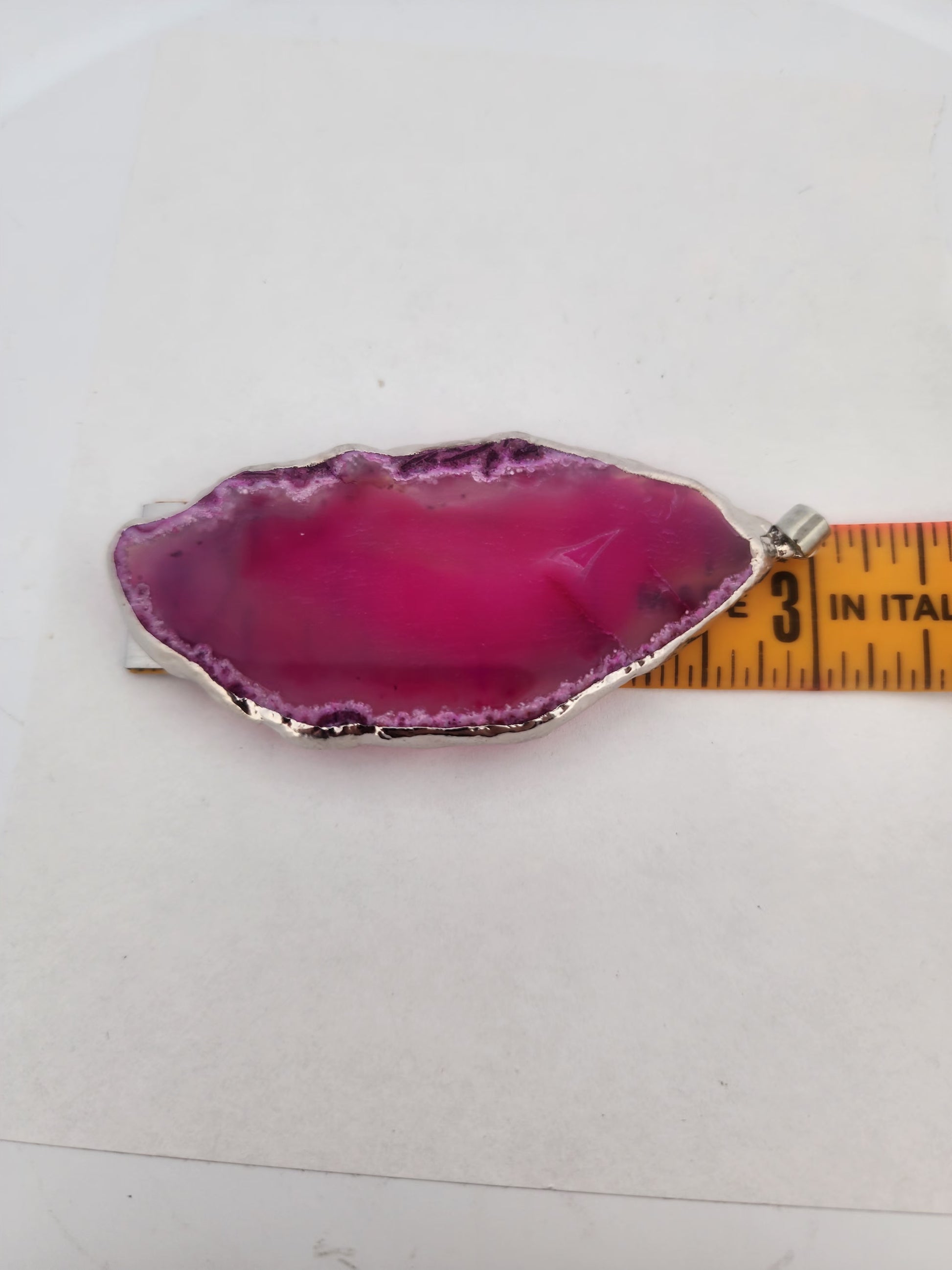 Pink agate slice with silver base on a white background, measured by a ruler.