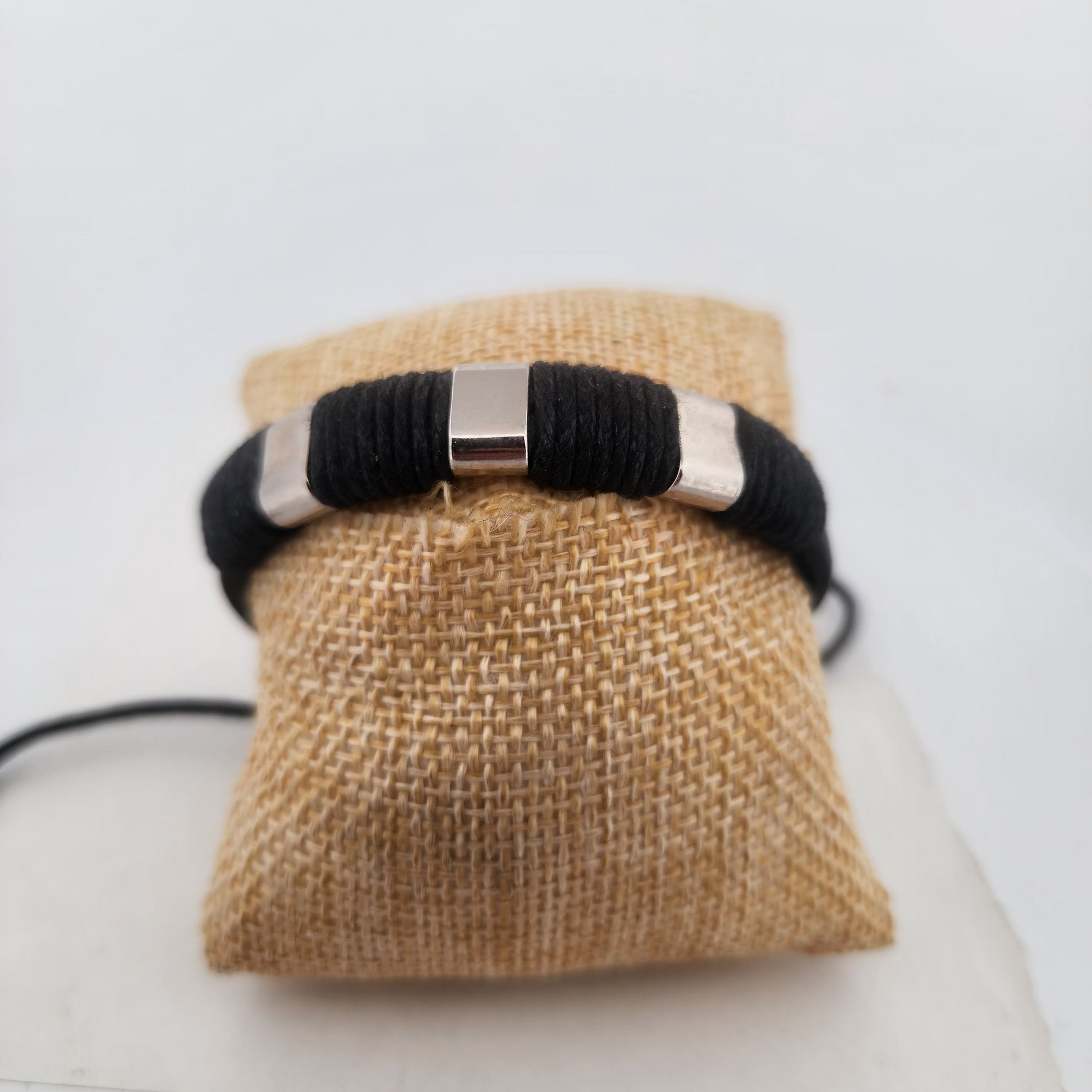 Black bracelet with a silver clasp on a burlap bag against a white background
