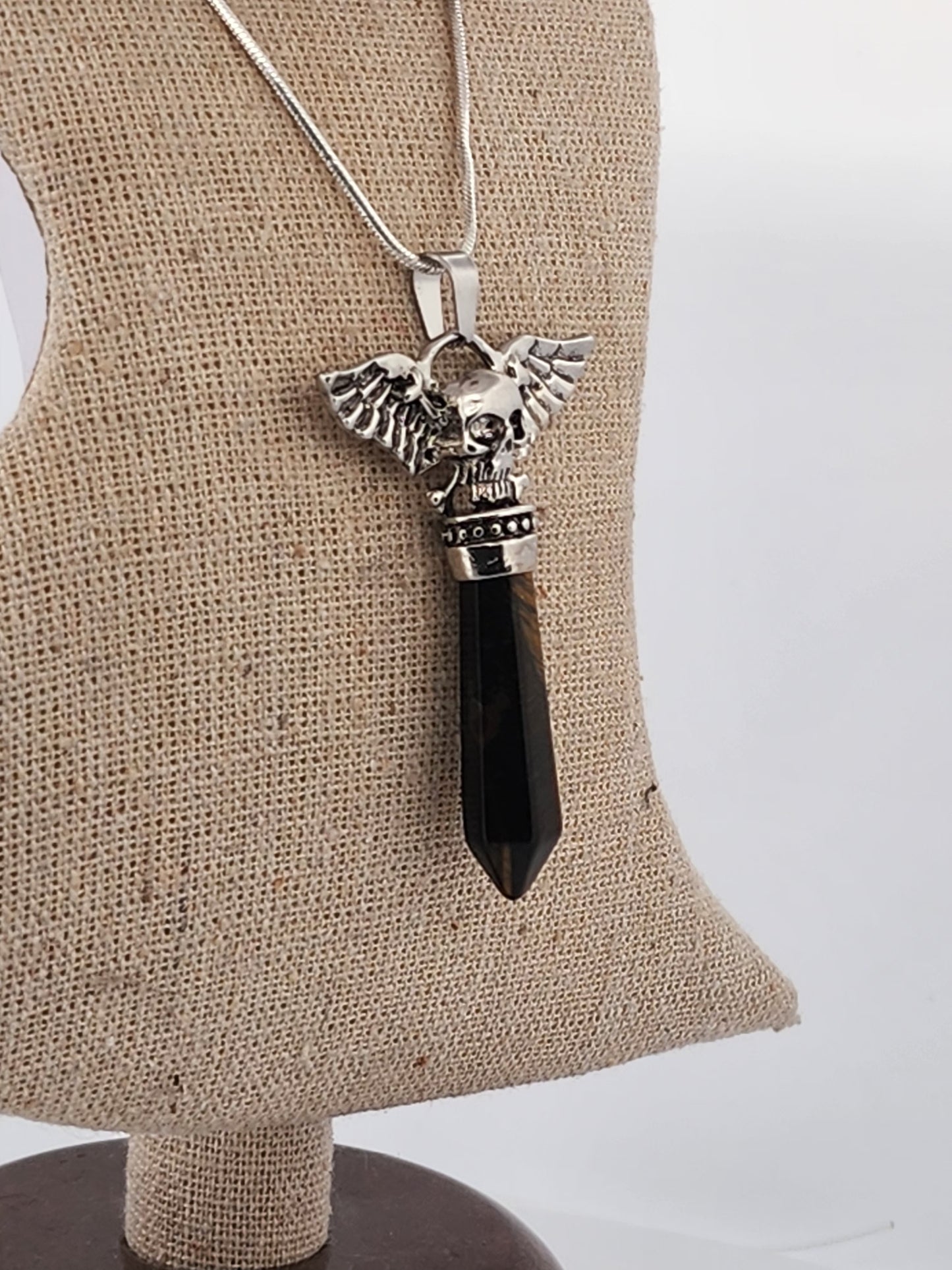 Necklace with a black pendant and silver angelic design on a beige stand.