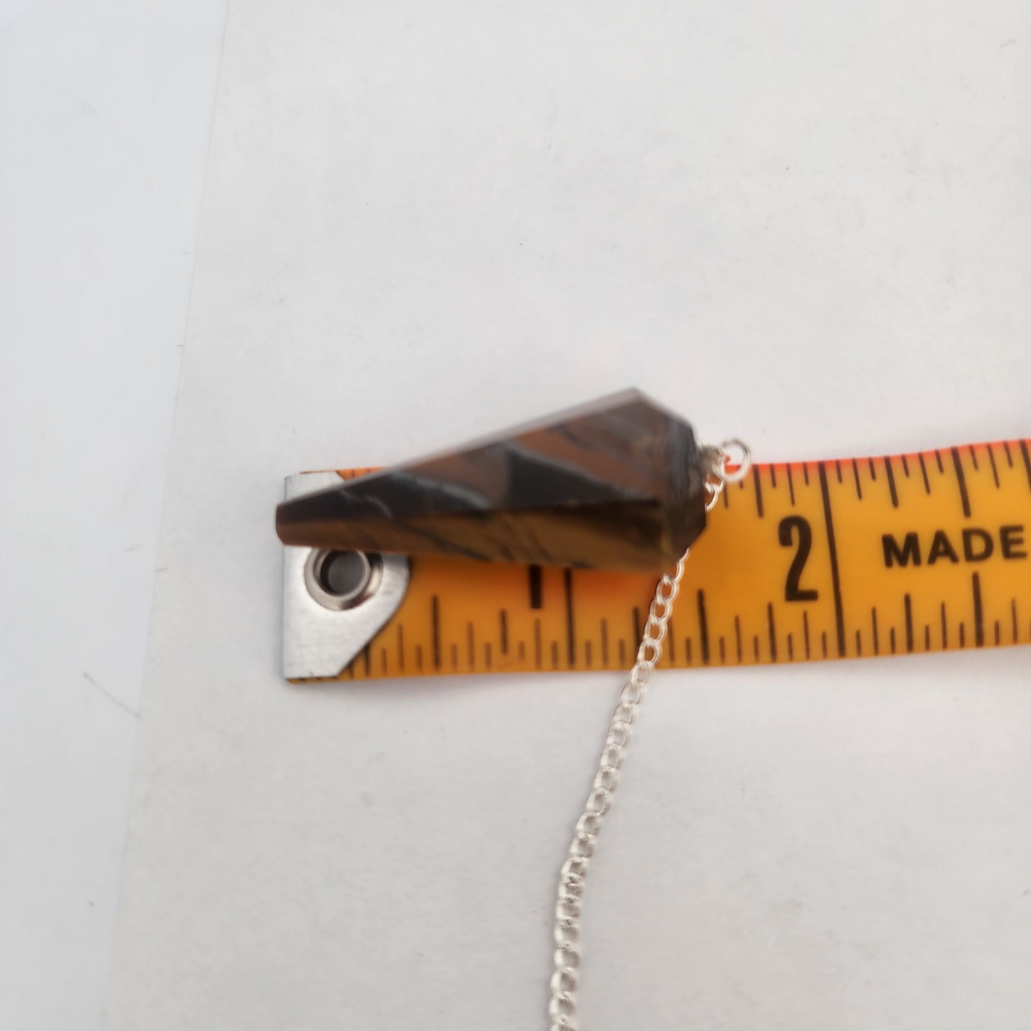 Small metal object with a chain next to a ruler on a white background