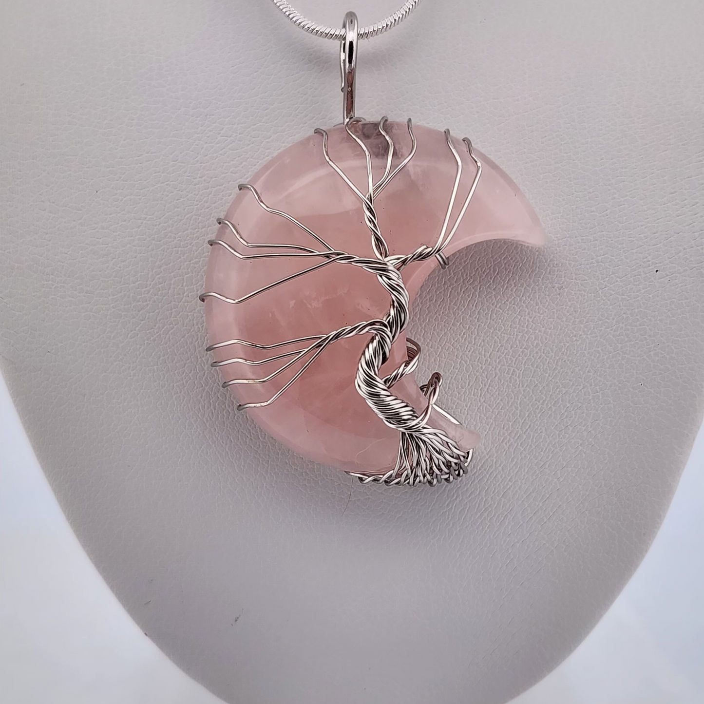 Pink stone pendant with silver tree design on a white stand