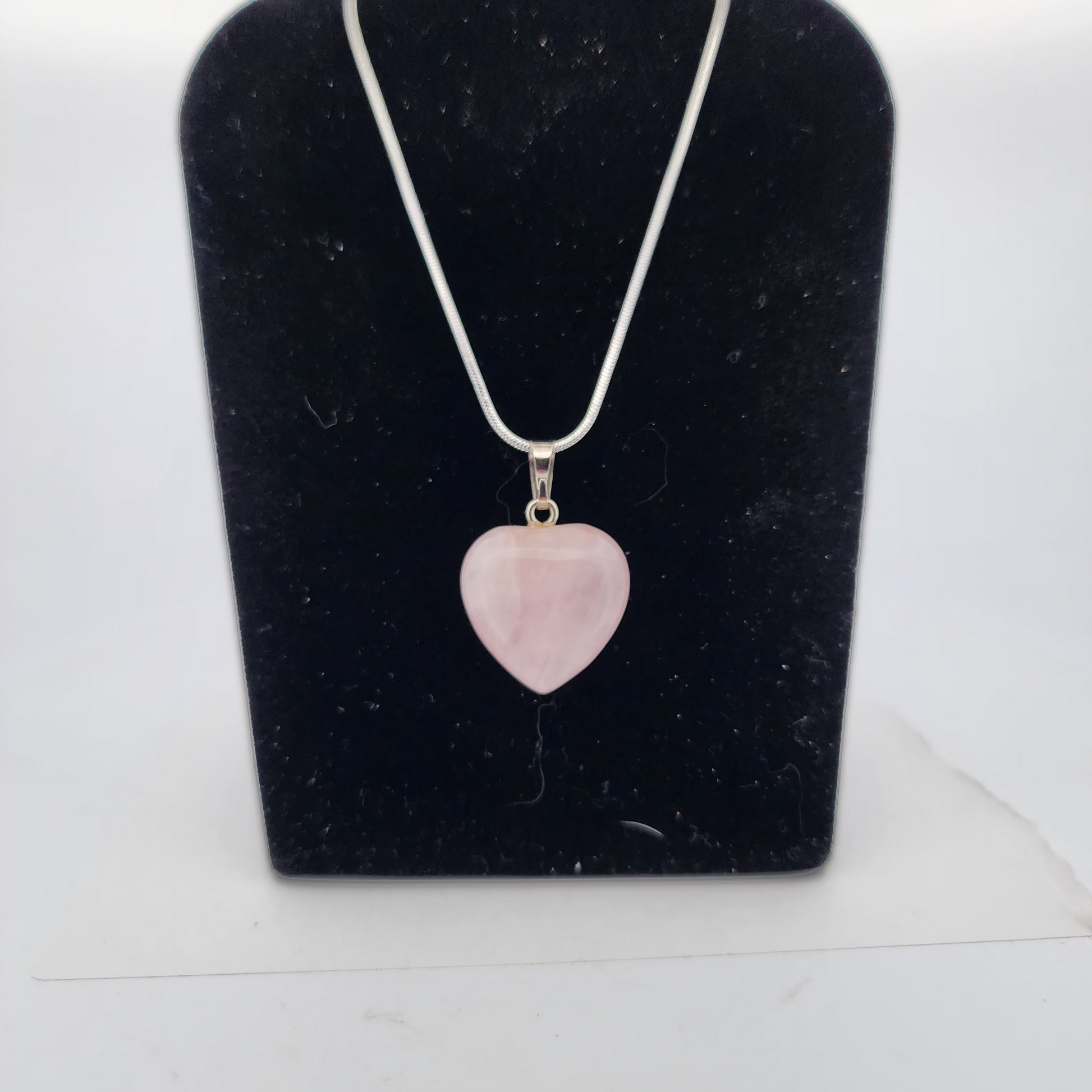 Necklace with a pink heart-shaped pendant on a black velvet stand.